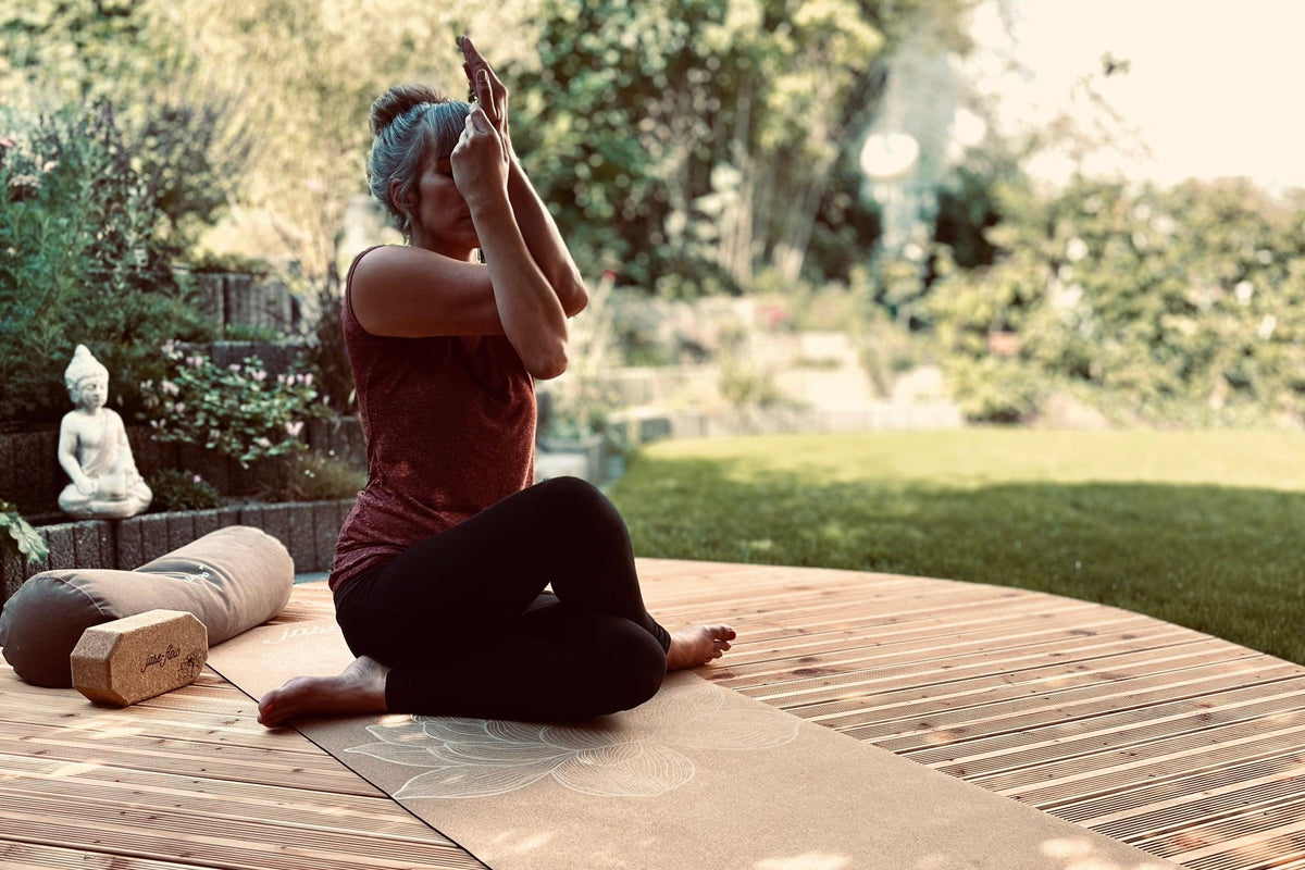 Yin-Yoga Lehrerin Jase mit der Asana Adlerarme auf der nachhaltigen Yogamatte Kork Lotus - mit Yogabolster und Yogablock aus Kork während dem Praktizieren
